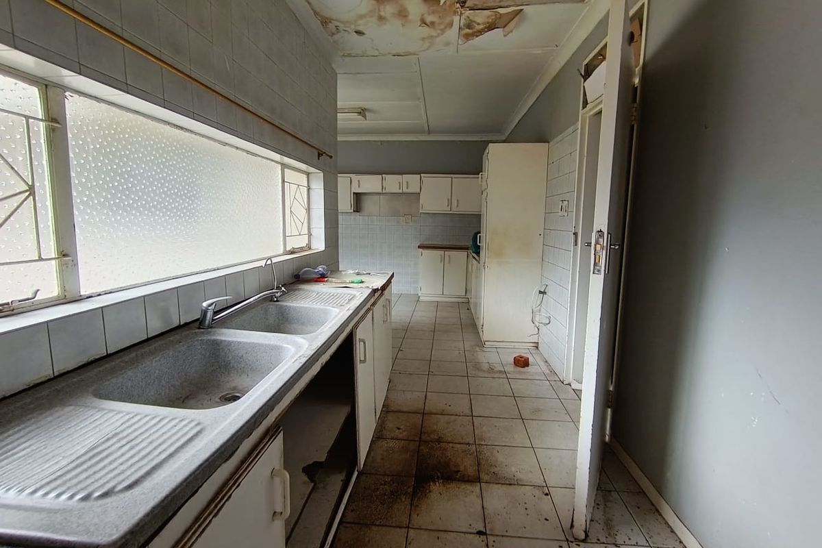 A dated kitchen area featuring a double basin sink, tiled flooring, and significant ceiling water damage requiring immediate repair and renovation.