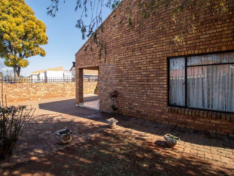 A rear exterior view of a face brick house featuring a paved courtyard, covered patio area, and secure boundary walling.