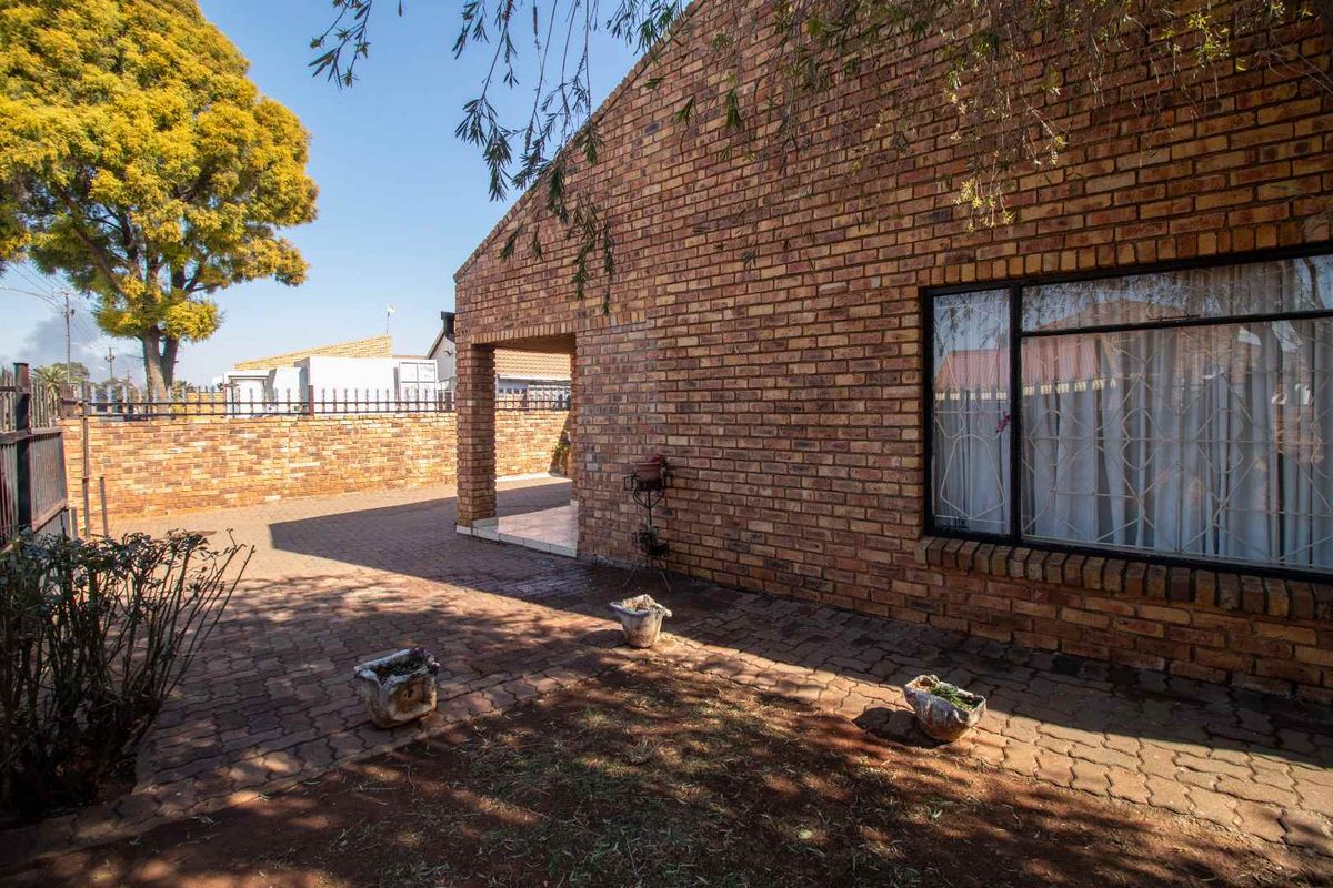 A rear exterior view of a face brick house featuring a paved courtyard, covered patio area, and secure boundary walling.