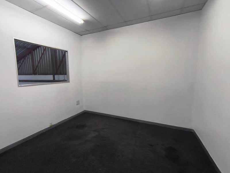 A vacant industrial office space featuring a drop ceiling, fluorescent lighting, and an internal window overlooking the warehouse area.