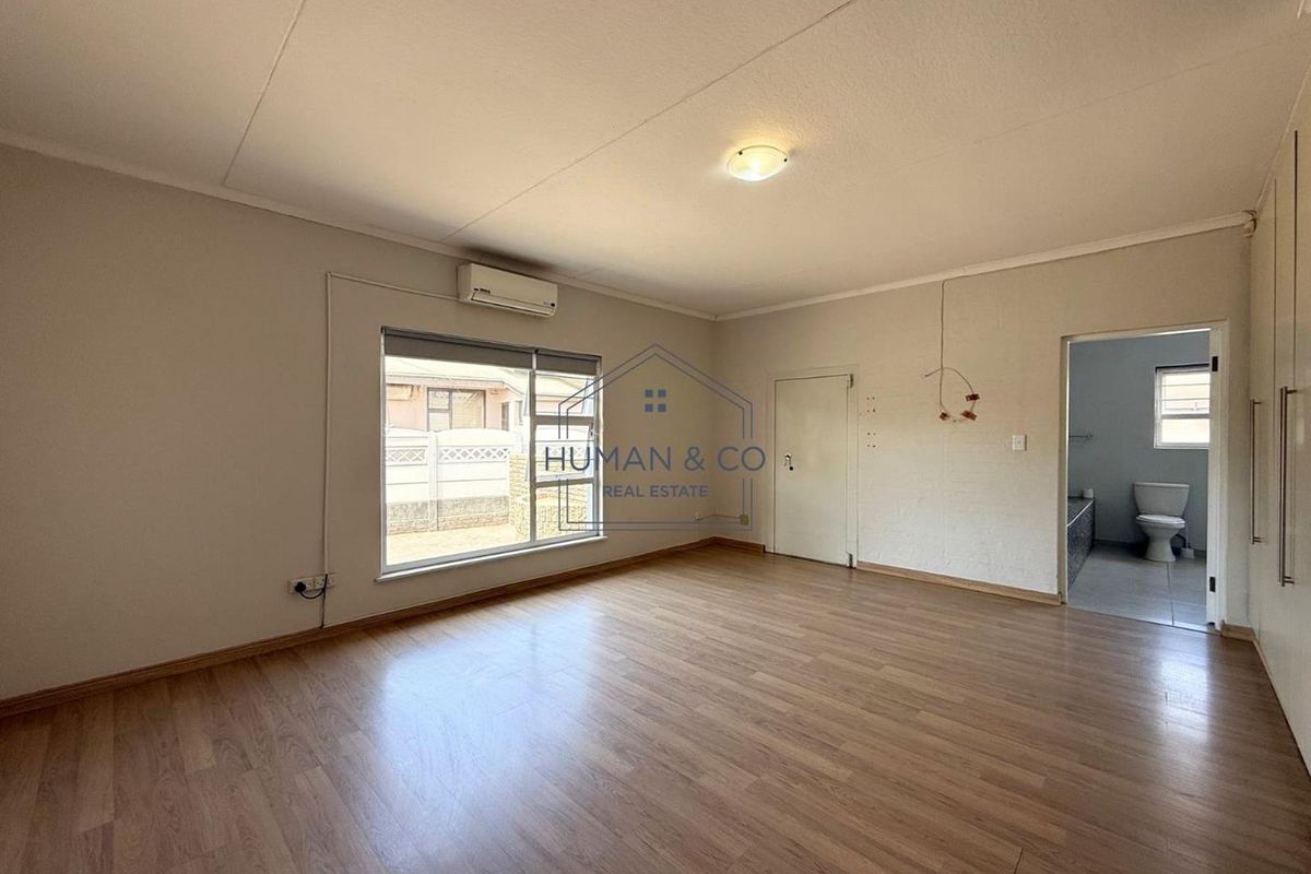 A spacious, empty bedroom featuring laminate flooring, a wall-mounted air conditioning unit, and an adjoining bathroom.