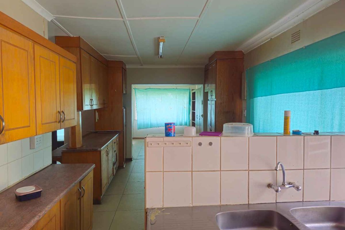 A dated kitchen featuring wooden cabinetry, laminate countertops, and a tiled sink area, offering a functional layout with potential for modernization.