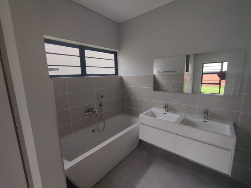 Modern bathroom featuring a sleek double vanity, a contemporary freestanding bathtub with handheld shower mixer, and large wall-mounted mirror.