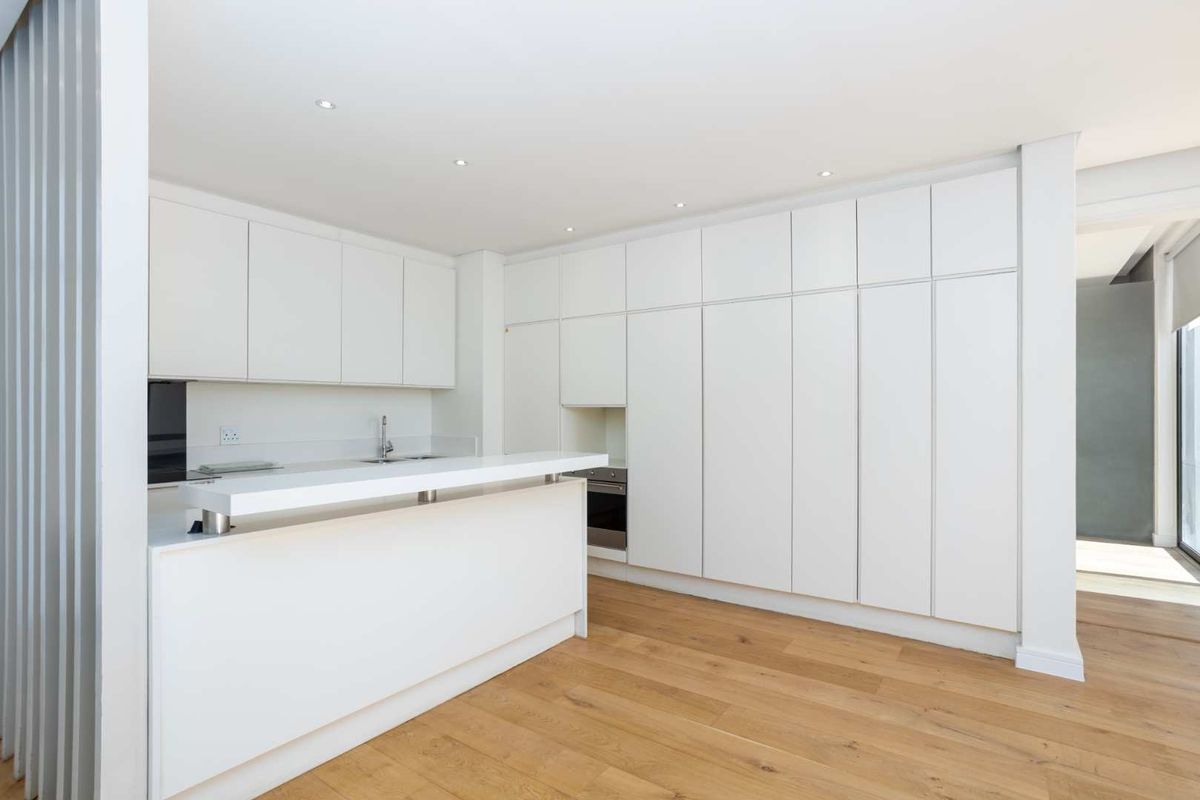 Modern minimalist kitchen featuring sleek white cabinetry, integrated oven, a functional breakfast bar island, and warm timber flooring.