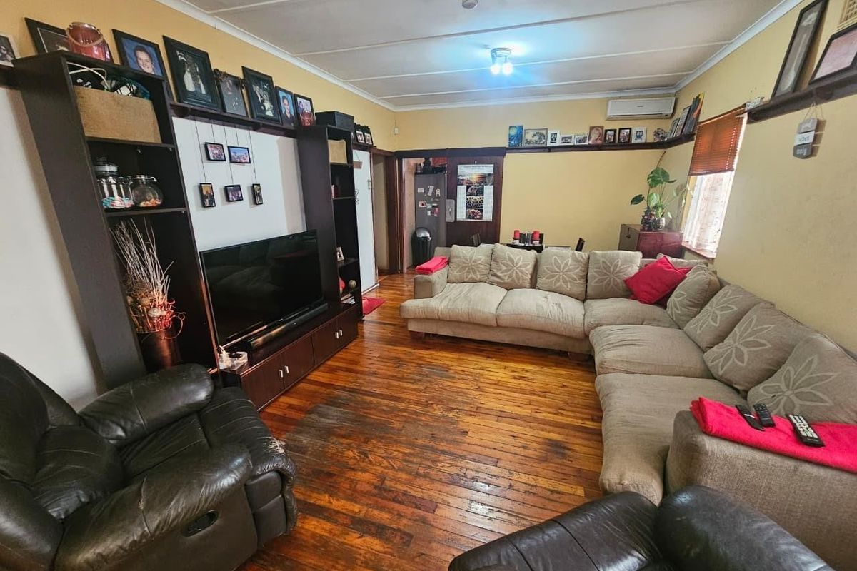 Spacious living room featuring original hardwood flooring, a built-in media shelving unit, and a wall-mounted air conditioning unit.