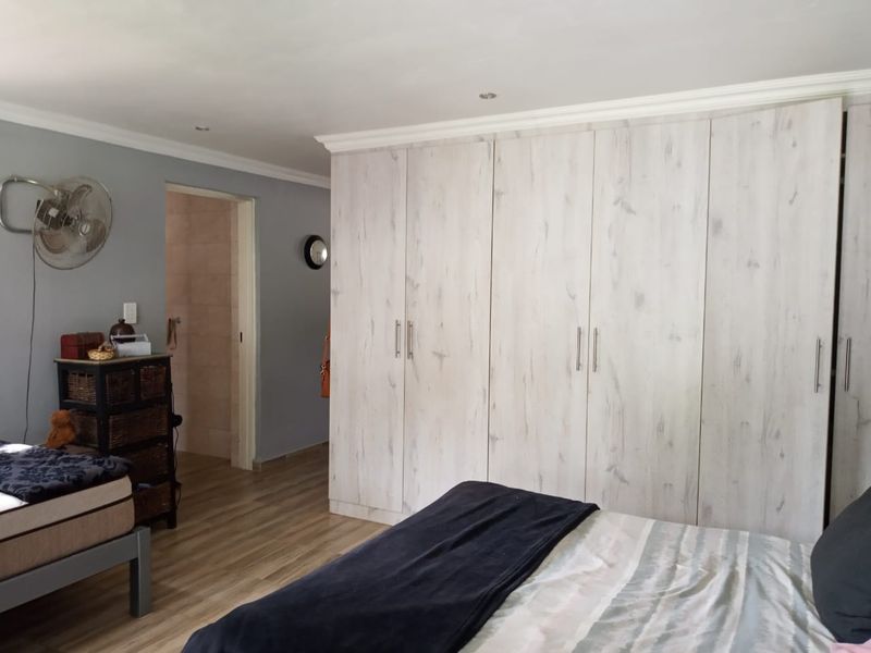 A well-maintained bedroom featuring light wood-look laminate flooring, extensive built-in cupboards with a modern finish, and recessed ceiling lighting.