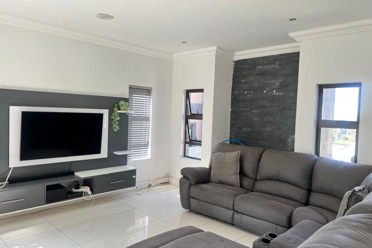 Modern living room featuring large format floor tiles, recessed downlighting, a built-in media console, and a decorative stone feature wall.