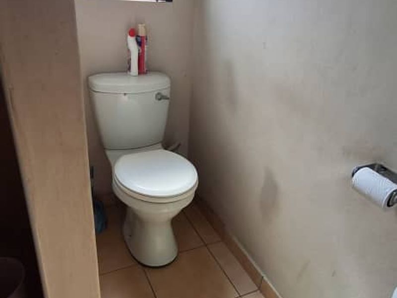 A compact bathroom featuring tiled flooring, a standard toilet, and a window with security bars. The space requires cosmetic updates to the wall finishes.