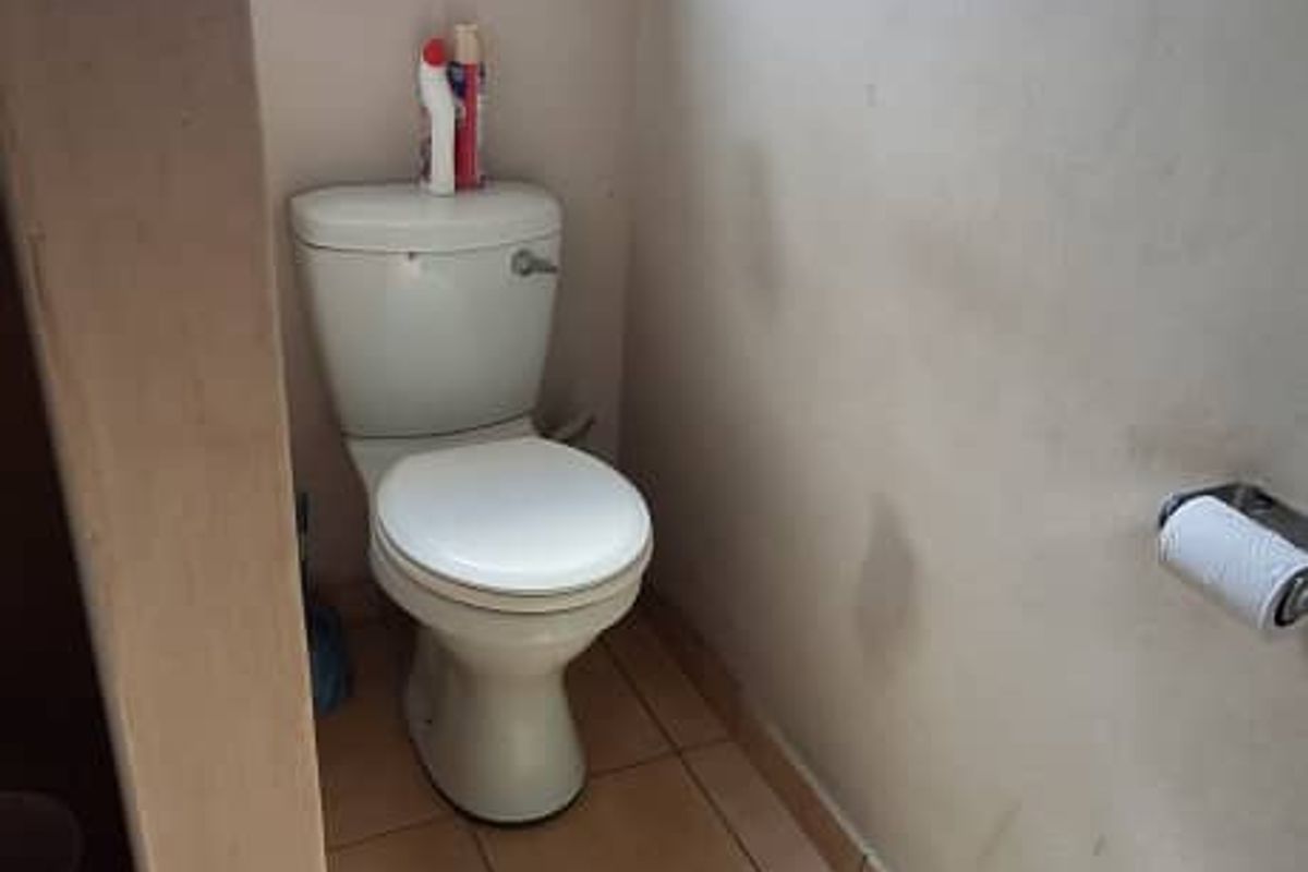 A compact bathroom featuring tiled flooring, a standard toilet, and a window with security bars. The space requires cosmetic updates to the wall finishes.