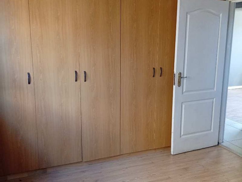 A bedroom featuring light wood-tone laminate flooring and extensive built-in wooden cupboards, offering ample storage space.