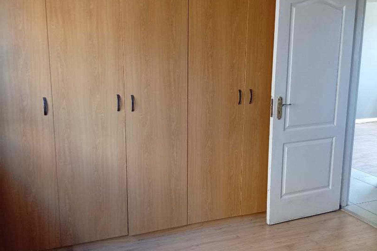 A bedroom featuring light wood-tone laminate flooring and extensive built-in wooden cupboards, offering ample storage space.