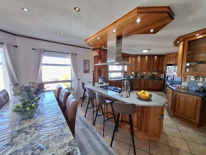 Spacious open-plan kitchen and dining area featuring extensive wooden cabinetry, granite countertops, a central breakfast bar, and integrated gas hob with extractor.