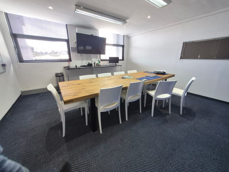 A functional office meeting room featuring patterned carpeting, built-in counter space, venetian blinds, and a combination of recessed and fluorescent lighting.