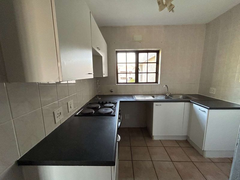 A functional kitchen featuring built-in cabinetry, dark laminate countertops, an electric hob, and a stainless steel sink with tiled finishes throughout.