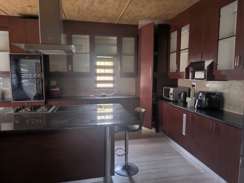 A functional kitchen featuring dark wood cabinetry, granite countertops, a central island with a gas hob, and integrated appliances.