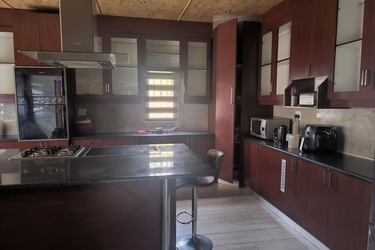 A functional kitchen featuring dark wood cabinetry, granite countertops, a central island with a gas hob, and integrated appliances.