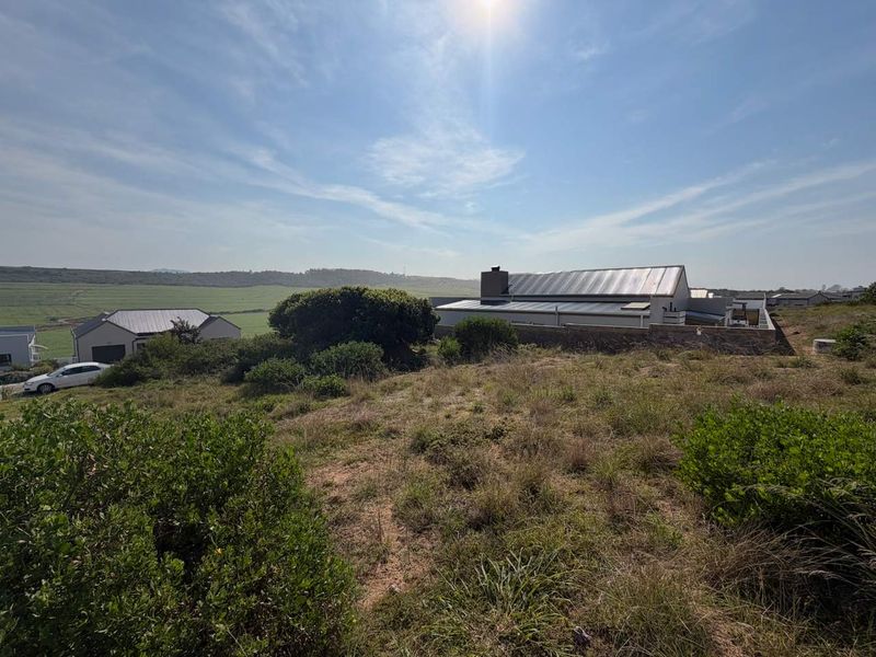 A wide-angle view of the vacant residential land, showcasing the surrounding natural landscape and neighboring residential properties under a clear sky.