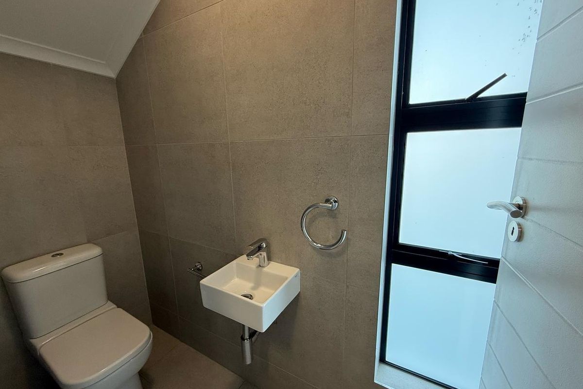 A modern guest bathroom featuring floor-to-ceiling neutral tiling, a wall-mounted basin, and a sleek toilet with a frosted glass window.