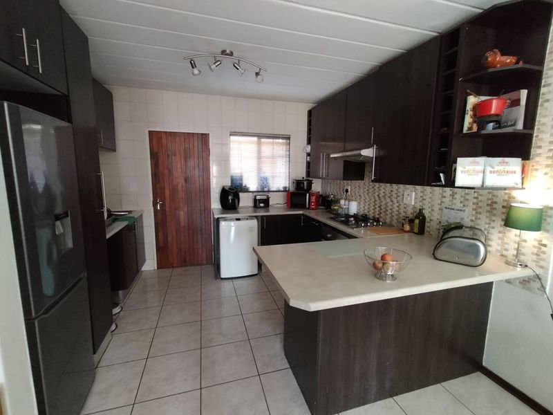 A functional kitchen featuring dark wood cabinetry, laminate countertops, tiled backsplash, and tiled flooring, offering a practical layout for daily meal preparation.