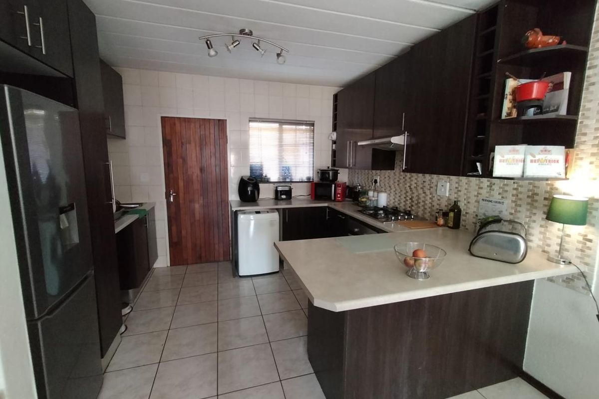 A functional kitchen featuring dark wood cabinetry, laminate countertops, tiled backsplash, and tiled flooring, offering a practical layout for daily meal preparation.