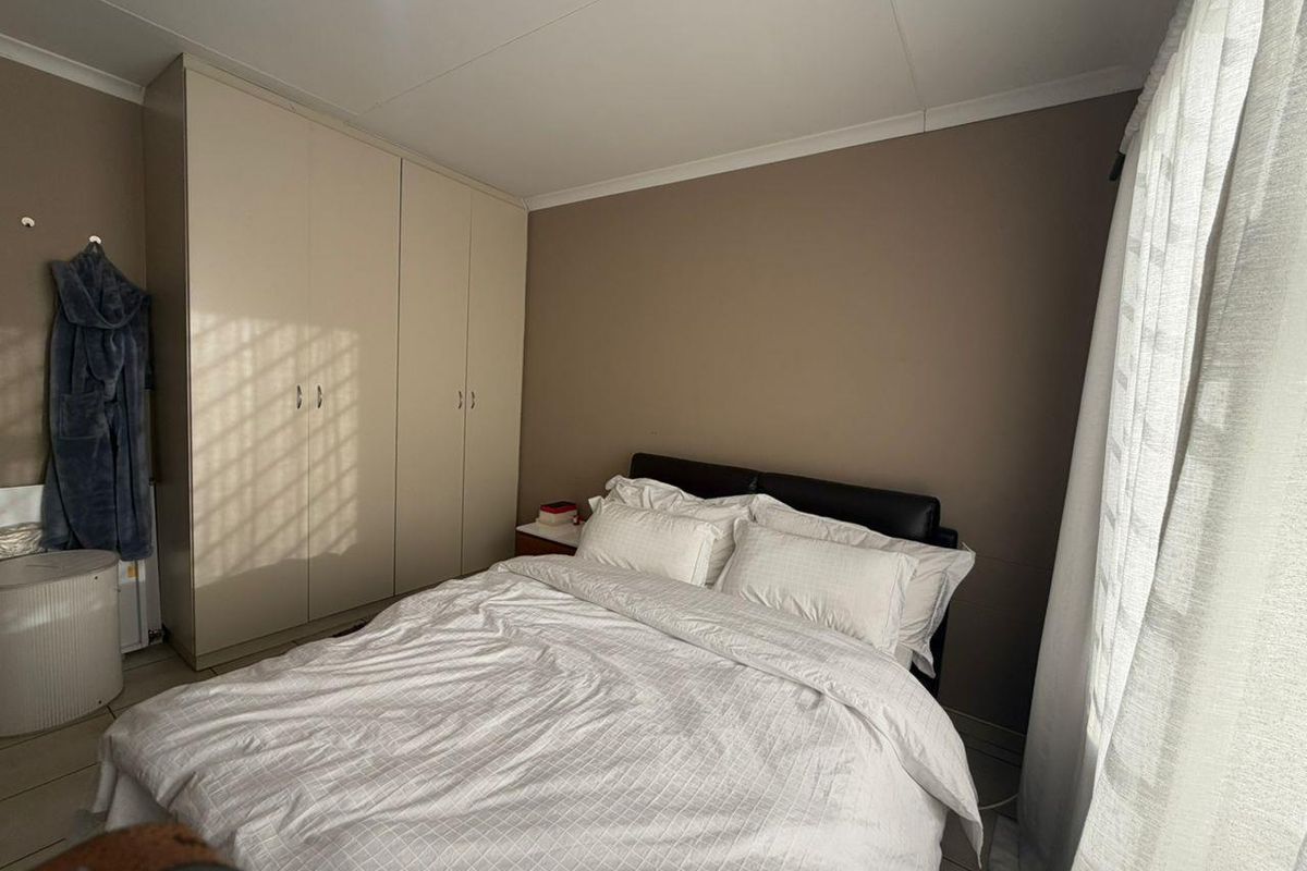 A bedroom featuring built-in floor-to-ceiling wardrobes, neutral wall tones, and tiled flooring, providing a functional and tidy sleeping space.