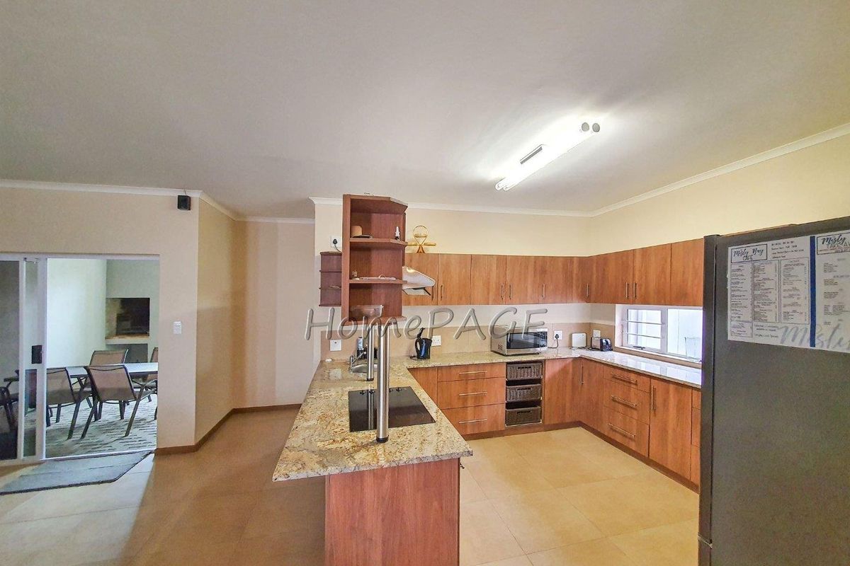 Spacious kitchen featuring wood-finish cabinetry, granite countertops, a central island with a built-in hob, and tiled flooring.