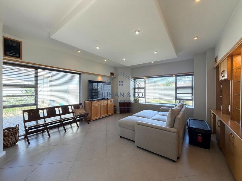 Spacious living room featuring tiled floors, recessed ceiling with downlights, and extensive built-in cabinetry, with large windows providing ample natural light.