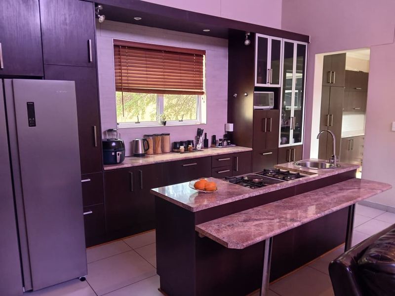 Modern kitchen featuring dark cabinetry, stone countertops, a central island with a gas hob, and integrated appliances, offering a functional and stylish cooking space.