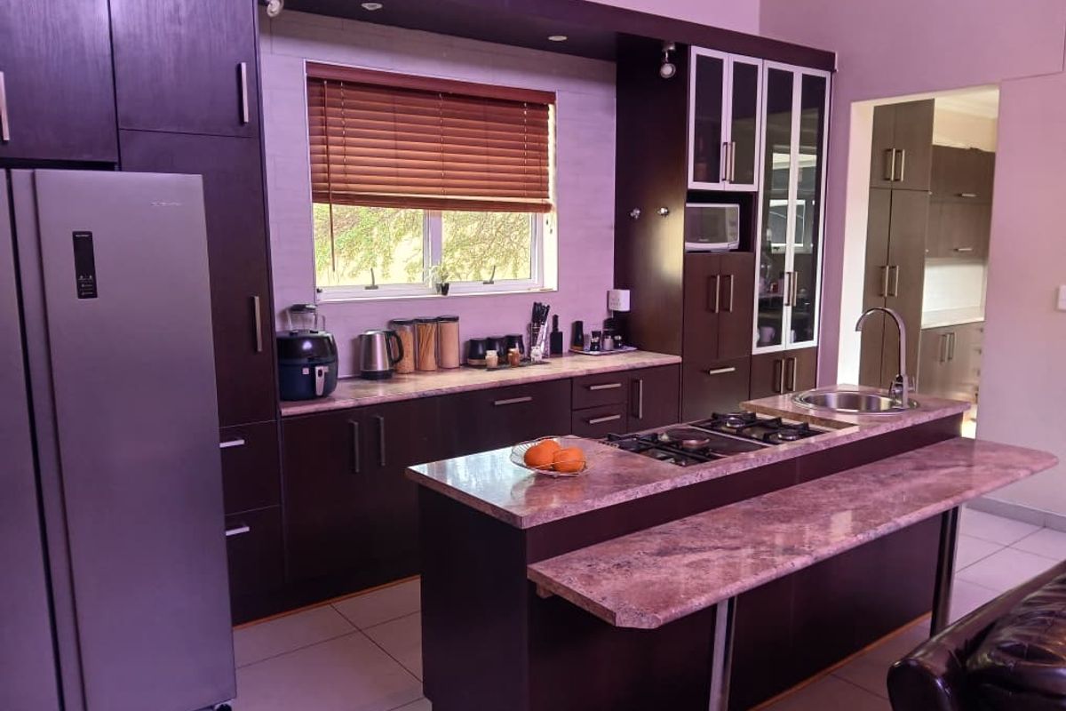 Modern kitchen featuring dark cabinetry, stone countertops, a central island with a gas hob, and integrated appliances, offering a functional and stylish cooking space.
