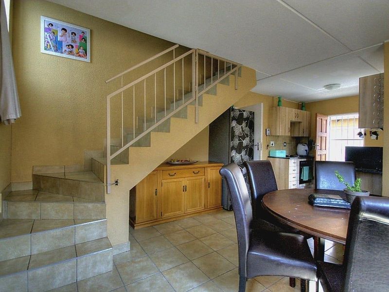 Open-plan living and dining area featuring tiled flooring, a staircase with metal balustrade, and an integrated kitchen space.