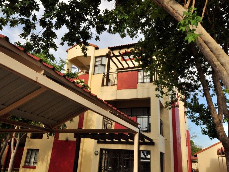 Exterior view of a multi-story apartment building featuring balconies, a pergola structure, and a covered carport area.