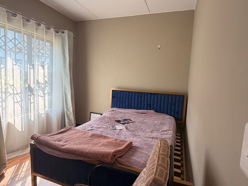 A bedroom featuring laminate flooring and a window fitted with a security gate, offering a functional space ready for cosmetic updates.