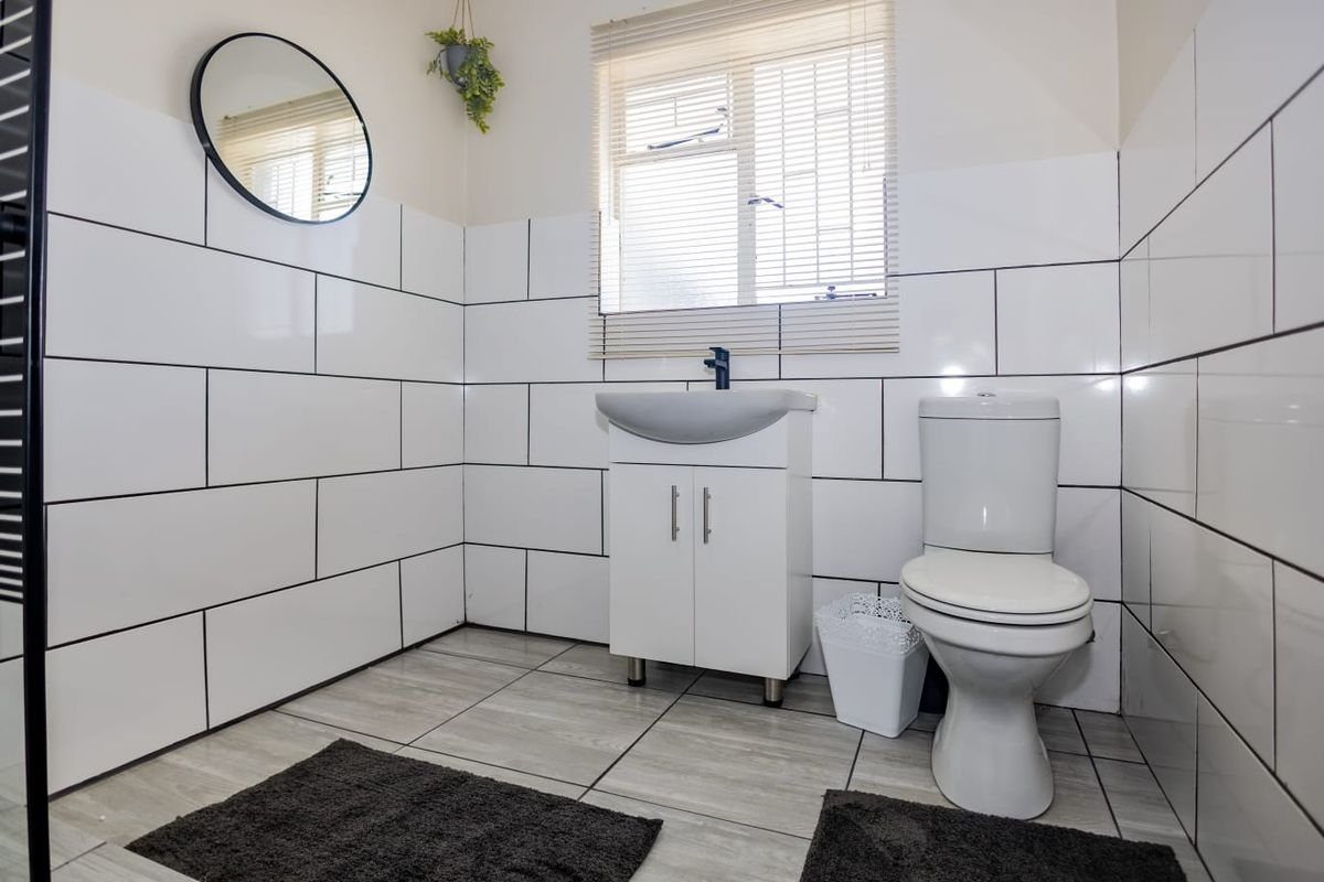A clean, modern bathroom featuring white subway-style wall tiles, a vanity basin, and a standard toilet.