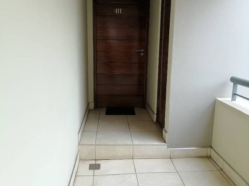 A clean and well-maintained apartment entrance area featuring tiled flooring, a solid wood front door, and a metal balustrade.