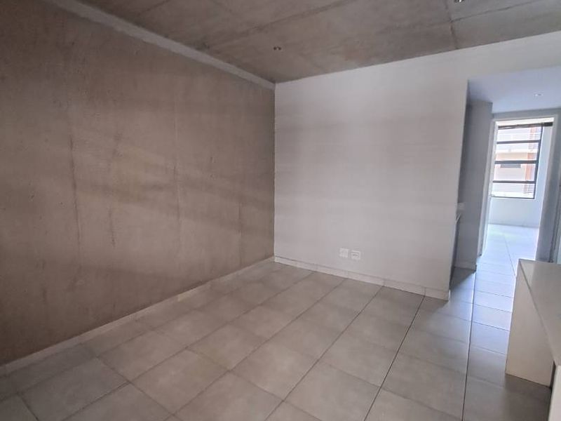 An empty living area featuring an exposed concrete ceiling and neutral tiled flooring, offering a modern industrial aesthetic.
