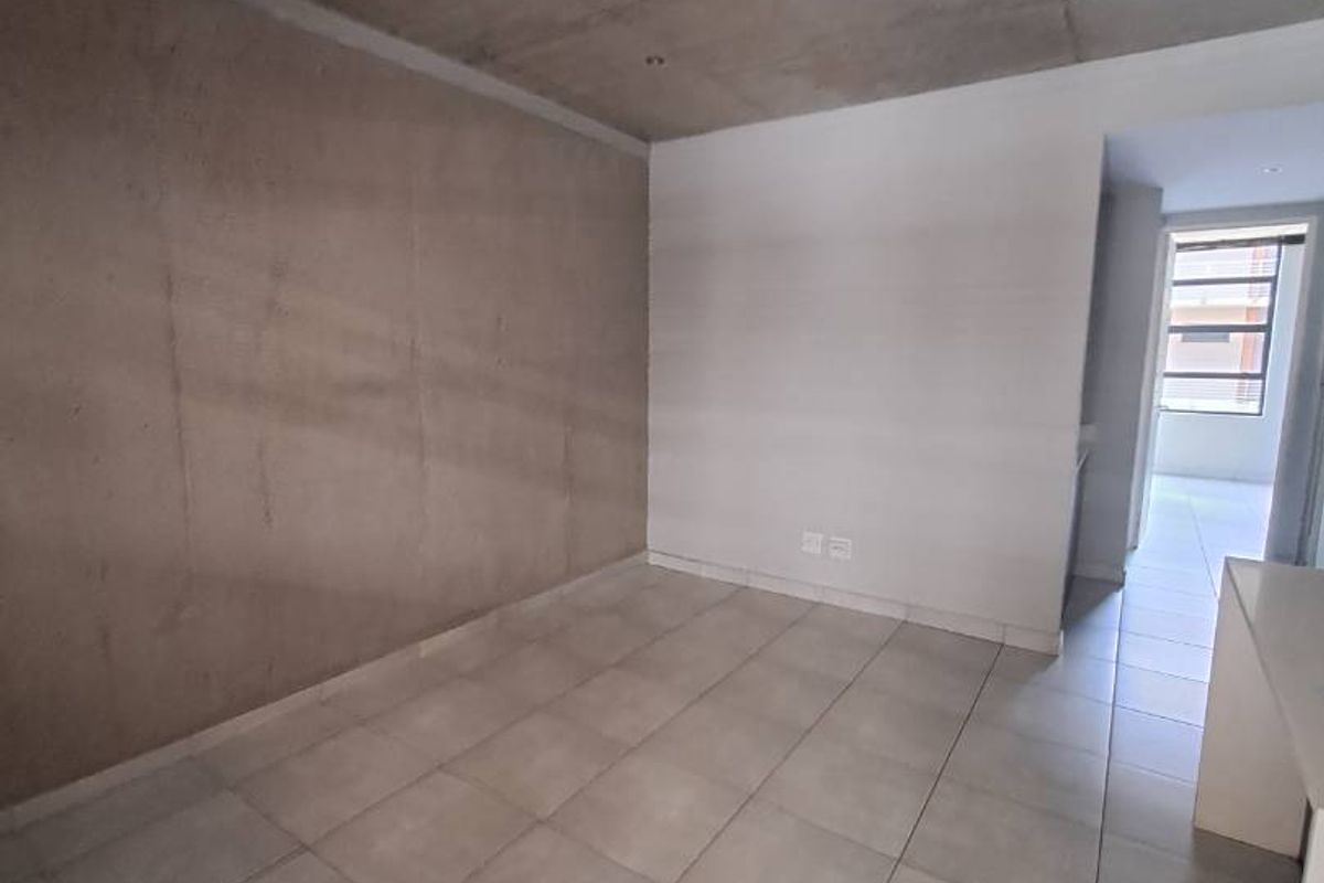 An empty living area featuring an exposed concrete ceiling and neutral tiled flooring, offering a modern industrial aesthetic.