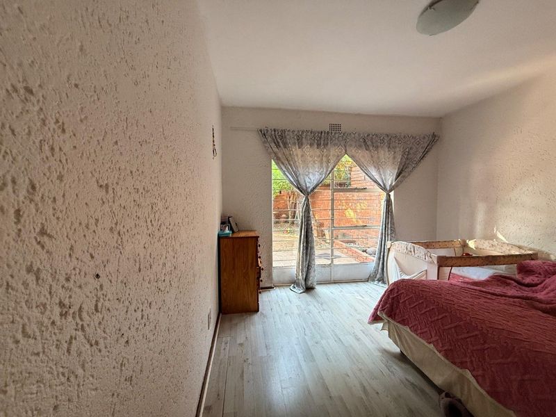 A bedroom featuring textured walls, laminate flooring, and a security gate leading to the exterior, providing a functional space with potential for modernization.
