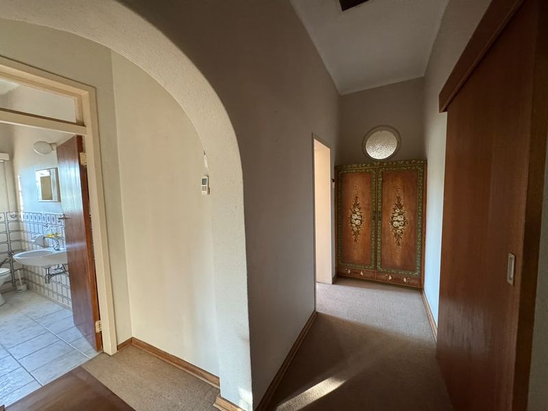 A hallway featuring an arched entryway, built-in cabinetry, and a circular window, connecting to an adjacent bathroom area.
