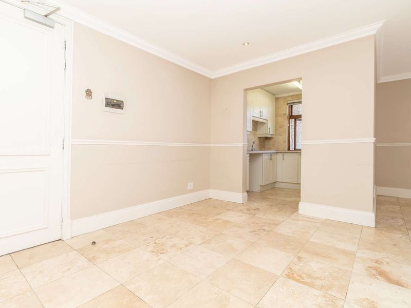 An open-plan living area featuring neutral walls, crown molding, chair rail detailing, and tiled flooring, with a direct view into the adjacent kitchen.
