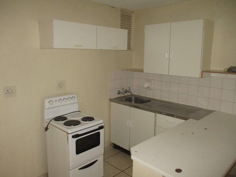 A compact, dated kitchen featuring basic white cabinetry, a stainless steel sink, tiled splashback, and a freestanding electric stove.