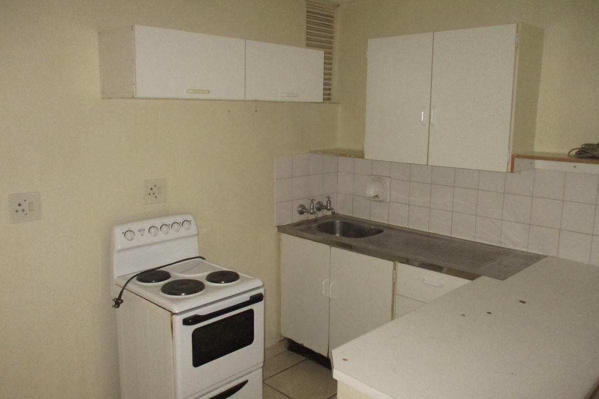 A compact, dated kitchen featuring basic white cabinetry, a stainless steel sink, tiled splashback, and a freestanding electric stove.
