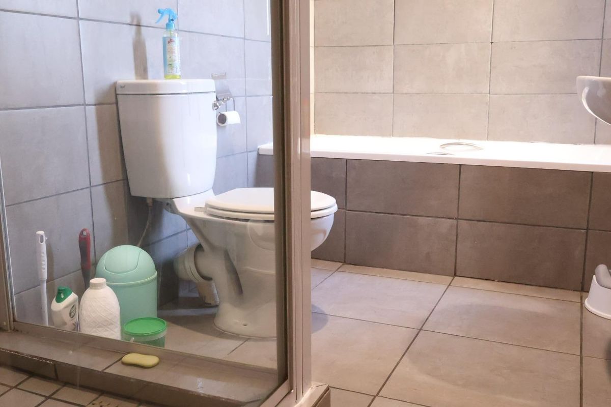 A functional bathroom featuring a bathtub, pedestal basin, and toilet with neutral grey wall and floor tiling.