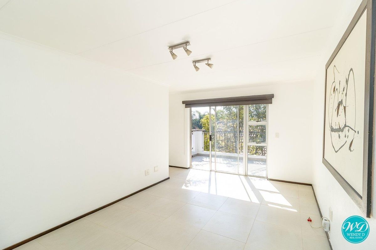 A bright, empty living room featuring neutral tiled flooring, track lighting, and a sliding glass door providing access to an outdoor balcony.