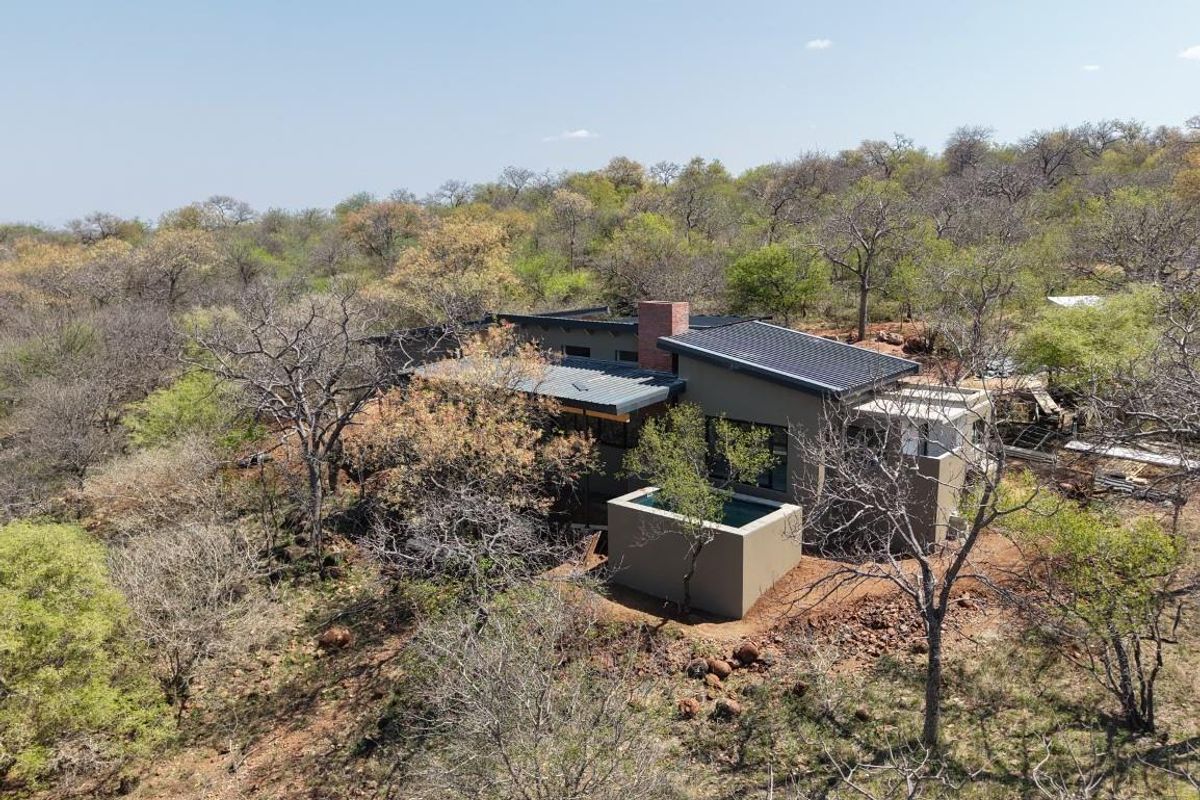 Aerial view of a modern bushveld home featuring a plunge pool, brick chimney, and contemporary architectural design set within a natural landscape.