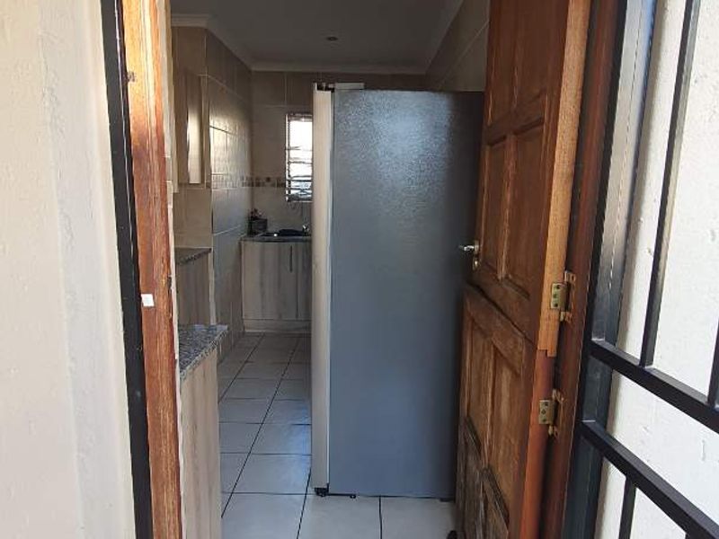 View through a security gate into a functional kitchen featuring tiled floors, granite countertops, and built-in cabinetry.