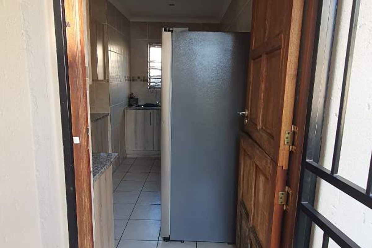 View through a security gate into a functional kitchen featuring tiled floors, granite countertops, and built-in cabinetry.