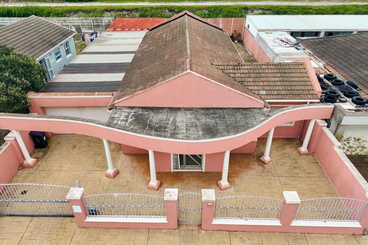 Aerial view of a detached house featuring a distinctive curved architectural facade, paved front courtyard, and perimeter wall with metal fencing.