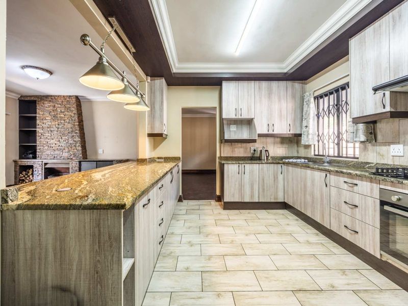 Modern kitchen featuring granite countertops, built-in oven, gas hob, and ample cabinetry, seamlessly flowing into an adjacent living area with a stone fireplace.