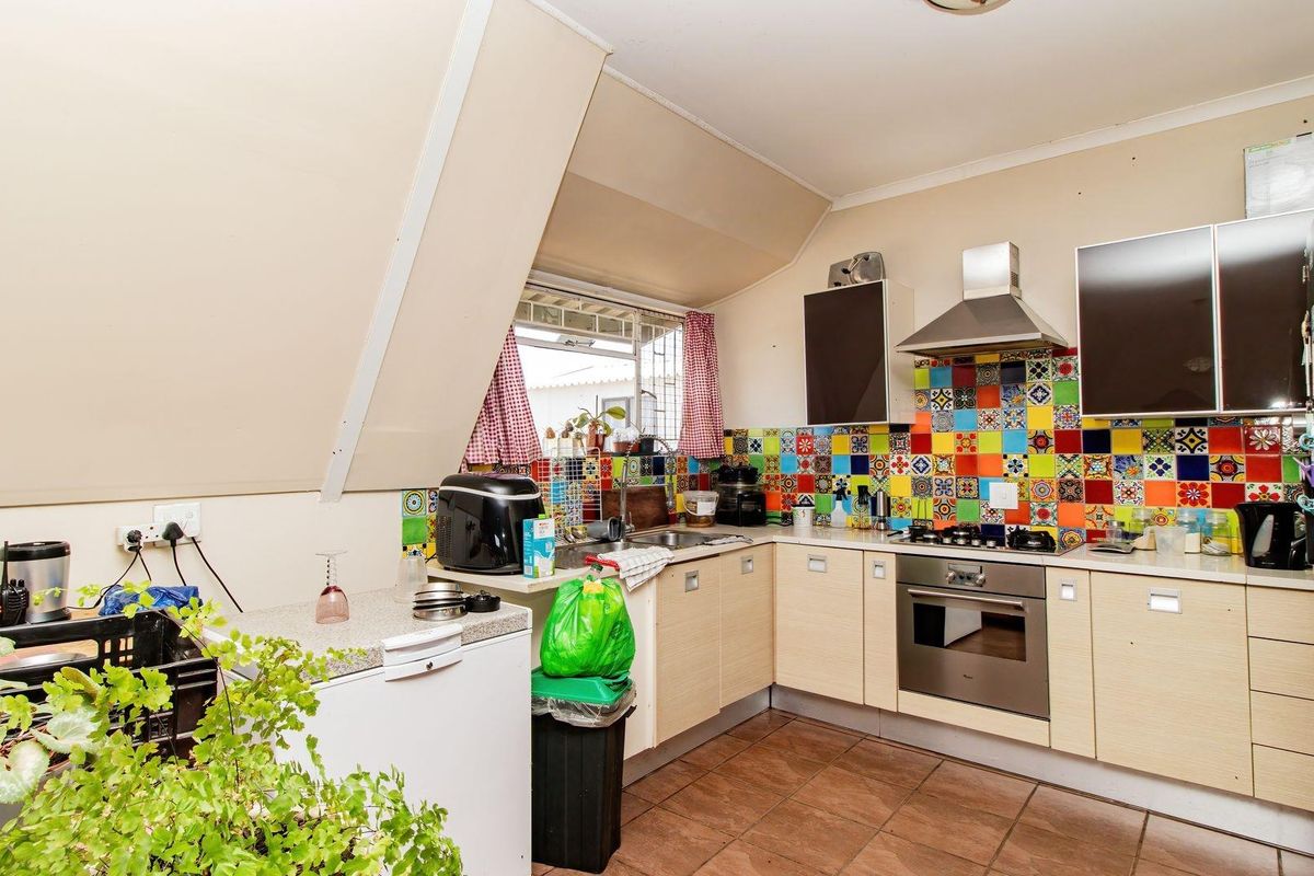 A functional kitchen featuring a colorful mosaic tile backsplash, built-in oven, stainless steel extractor fan, and tiled flooring under a sloped ceiling.