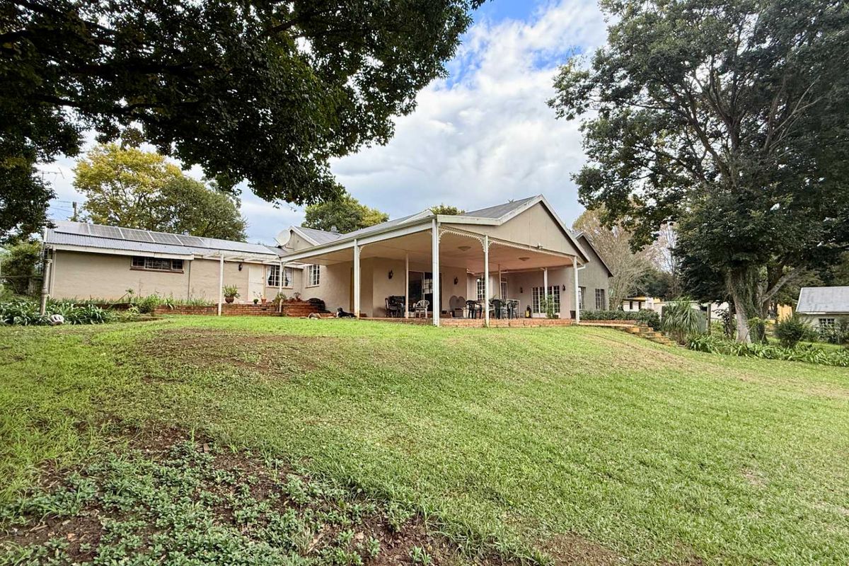 Rear view of the house featuring a spacious covered patio area, expansive lawn, and mature trees in a peaceful garden setting.